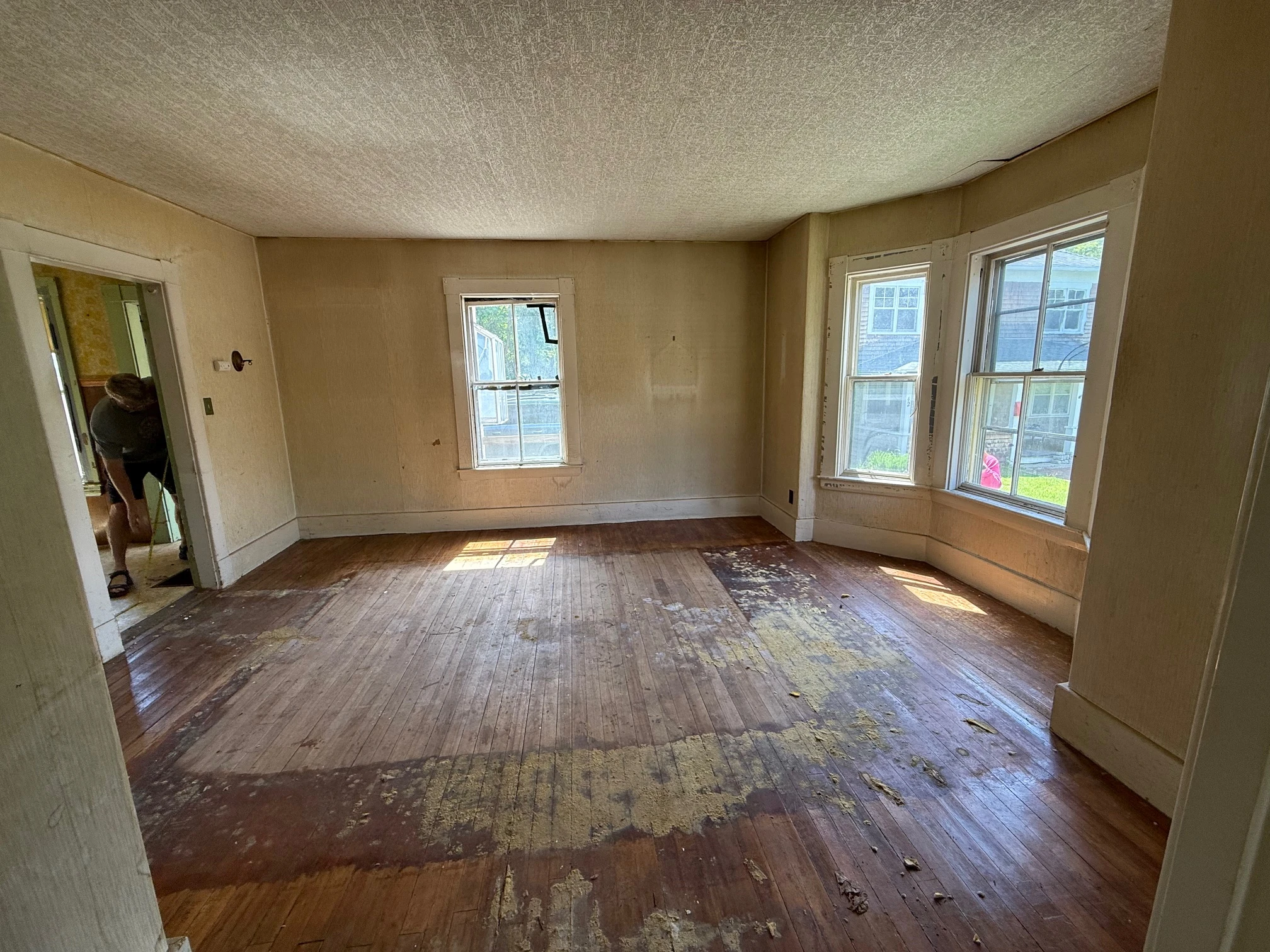 Large room with bay windows and worn flooring