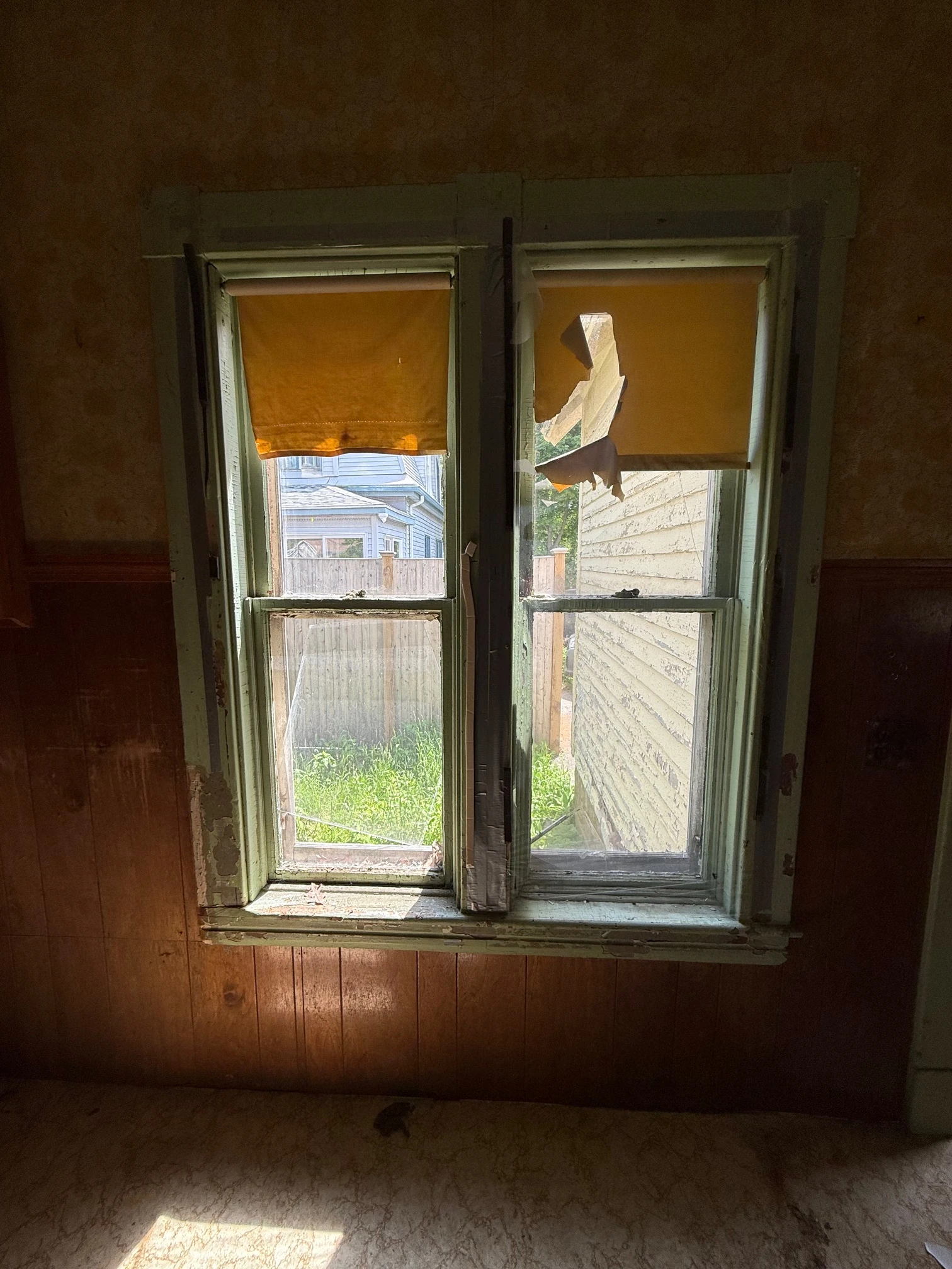 Paired windows with damaged shades and dark paneling